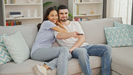 Poster - Beautiful couple finds joy in relaxing together, comfortably watching a movie, confidently commanding the remote from their sofa at home