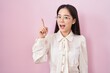 © Krakenimages.com - Young chinese woman standing over pink background pointing finger up with successful idea. exited and happy. number one.