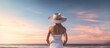 A woman wearing a white hat and a white dress is standing on a beach