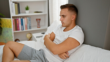 a young man in casual attire sits thoughtfully in a modern bedroom with bookshelf and decorative ite