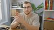 © Krakenimages.com - A confident young man with a beard and glasses sitting in a modern office, looking directly at the camera.