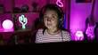 © Krakenimages.com - A young brunette woman wearing headphones in a colorful gaming room at night.