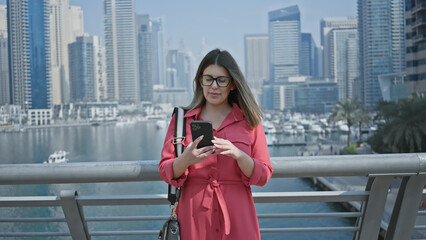 Sticker - Brunette woman in red uses smartphone against dubai marina skyline backdrop, embodying luxury, travel, and modernity.