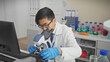 Asian man in lab coat using microscope in a modern laboratory indoors.