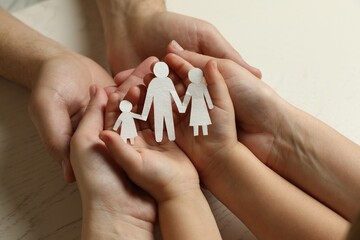 Wall Mural - Parents and child holding paper cutout of family at white wooden table, closeup