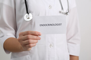 Endocrinologist with stethoscope holding card on light grey background, closeup