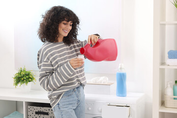 Poster - Happy woman pouring laundry detergent into cap near washing machine indoors