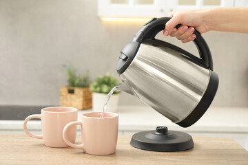 Wall Mural - Woman pouring hot water from electric kettle into cup in kitchen, closeup