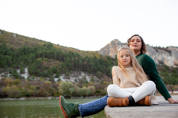 A happy mom  and daoghter have fun  against the background of a lake, forest and mountain. People breathes fresh healthy air. Outdoor weekend concept