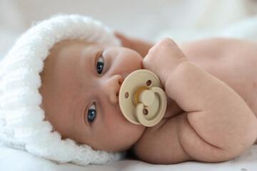 Sticker - Cute newborn baby in white knitted hat lying on bed, closeup