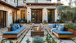 cozy outdoor living space. It features modern furniture with blue upholstered benches and cushions. The house has a light-colored exterior with wooden and glass-pane doors, and string lights
