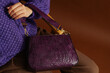 Autumn, winter fashion details. Close up photo of trendy purple  faux leather woven bag, purse in elegant outfit. Woman posing on brown background. Copy, empty, blank space for text