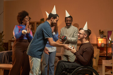 Side view portrait of adult man with disability celebrating Birthday party with friends presenting gifts and wearing caps