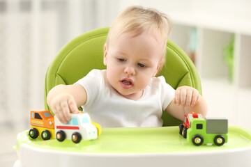children toys. cute little boy playing with toy cars in high chair at home