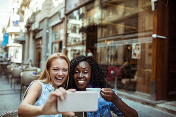 Wall Mural - Two young women taking selfie in street cafe