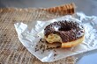 Un donut glaseado de chocolate con virutas reposa sobre un papel de aluminio arrugado, un mordisco revela su interior suave, un tentador manjar en un momento de indulgencia dichosa.