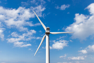 A symbol of renewable energy, an electric generating wind mill against a blue summer sky with white clouds