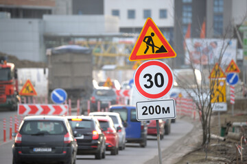 Wall Mural - Roadworks warning traffic signs of construction work on city street and slowly moving cars