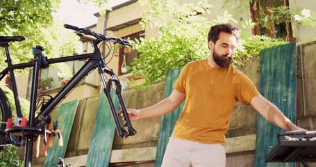 Sports enthusiast man using professional wrench for adjusting bike front fork. Active male cyclist disengaging broken wheel in the yard and using specialized work tool for repairing bicycle.