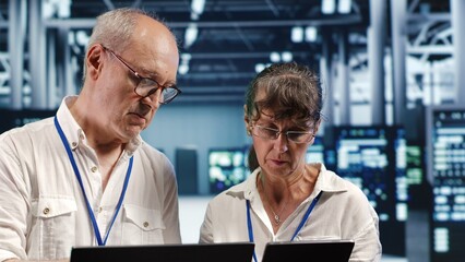Poster - coworkers looking around high tech data center, using laptop and tablet to crosscheck disaster recov