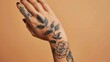 Female hand with floral tattoo design, artistically displayed against solid backdrop, emphasizing detail and artistry of black ink body art. Personal expression and body art.