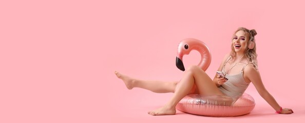 Wall Mural - Happy young woman in swimsuit and inflatable ring listening to music on pink background with space for text