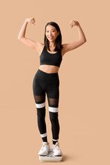 Sticker - Beautiful young Asian woman with scales showing muscles on beige background. Weight loss concept