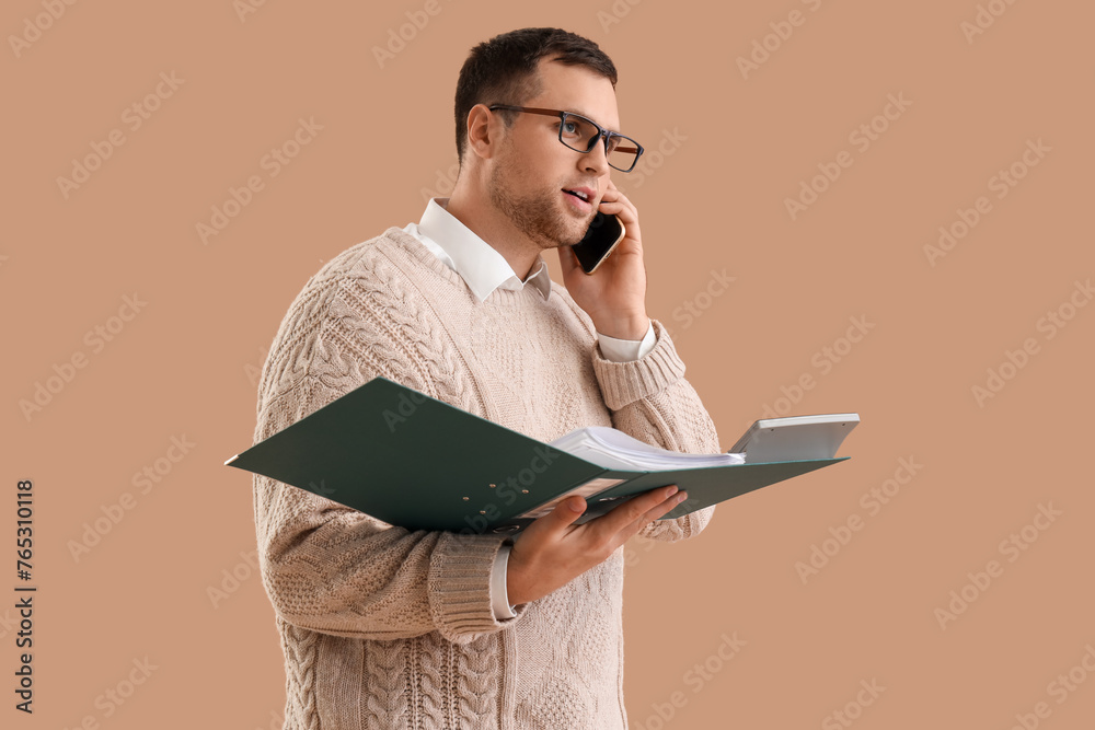 Male accountant with folder talking by mobile phone on brown background