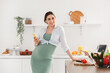 Young pregnant woman with mobile phone cooking in kitchen