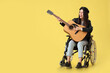 © Pixel-Shot - Female artist in wheelchair with guitar singing on yellow background