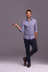 Poster - Happy man, portrait and presentation with palm for advertising, marketing or showcase on a gray studio background. Young and handsome male person or employee with smile showing option on mockup space