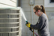 A woman is spraying water on an air conditioner