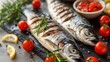  A few fishes resting atop a slicing board near a plate of juicy tomatoes and squeezed lemons