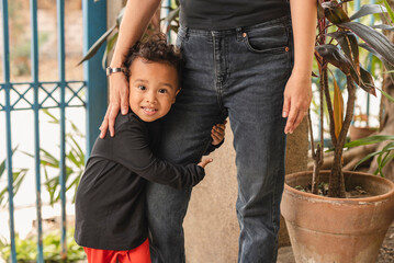 adorable asian toddler hugging mother's leg lovingly outdoors