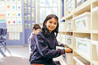 © Austockphoto - Student pulling her books out of a tray in the classroom smiling