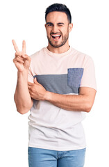 Wall Mural - Young handsome man wearing casual clothes smiling with happy face winking at the camera doing victory sign. number two.