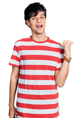 Sticker - Handsome hipster young man wearing casual striped t shirt smiling with happy face looking and pointing to the side with thumb up.