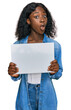 Beautiful african young woman holding blank empty banner scared and amazed with open mouth for surprise, disbelief face