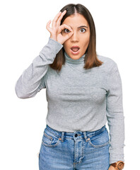 Wall Mural - Young beautiful woman wearing casual turtleneck sweater doing ok gesture shocked with surprised face, eye looking through fingers. unbelieving expression.