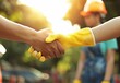 Close up of two construction workers shaking hands with other people in the background, sunny day, worker wearing a yellow helmet holding out his hand for a handshake, outdoor setting