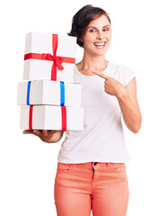 Canvas Print - Beautiful young woman with short hair holding gifts smiling happy pointing with hand and finger