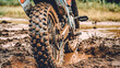 A dirty motorcycle tire is shown in mud. The tire is covered in mud and dirt, and it is in a muddy field