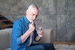 © brizmaker - Mature man holding glass with water and taking tablet from headache