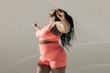 © gstockstudio - Full length of active African plus size woman in sportswear doing stretching exercises in fitness studio