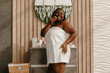 © gstockstudio - Happy plus size African woman covered in towel enjoying beauty treatment at the domestic bathroom