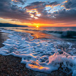 Sunrise kisses the ocean's edge, casting a glow on frothy waves against the pebbled shore.