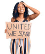 Young african american woman holding united we stand banner stressed and frustrated with hand on head, surprised and angry face