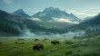 Bison graze in a misty green valley with towering mountains and clear morning skies in the background.
