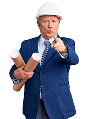 Canvas Print - Senior handsome grey-haired man wearing architect hardhat holding blueprints pointing with finger to the camera and to you, confident gesture looking serious