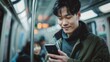 Young asian handsome man looking on smatrphone in subway train